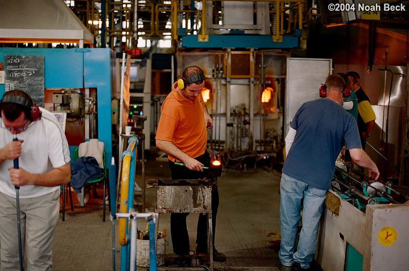 July 6, 2004: The craftsman on the left is blowing a piece into shape in a mold below the floor. The other two are preparing molten crystal to be blown.